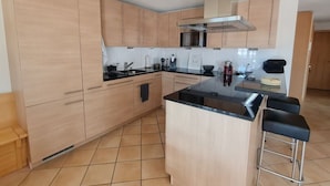 Una cocina moderna con armarios de madera clara, encimera negra y campana extractora de acero inoxidable.