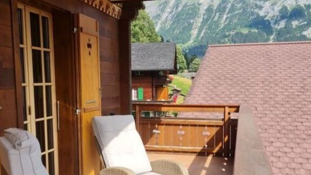 Un edificio de madera con un balcón que tiene sillas de mimbre y una mesa.