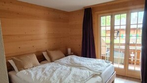 Un dormitorio con paneles de madera, una cama grande, un puerta corrediza de vidrio a un balcón y una lámpara de techo.