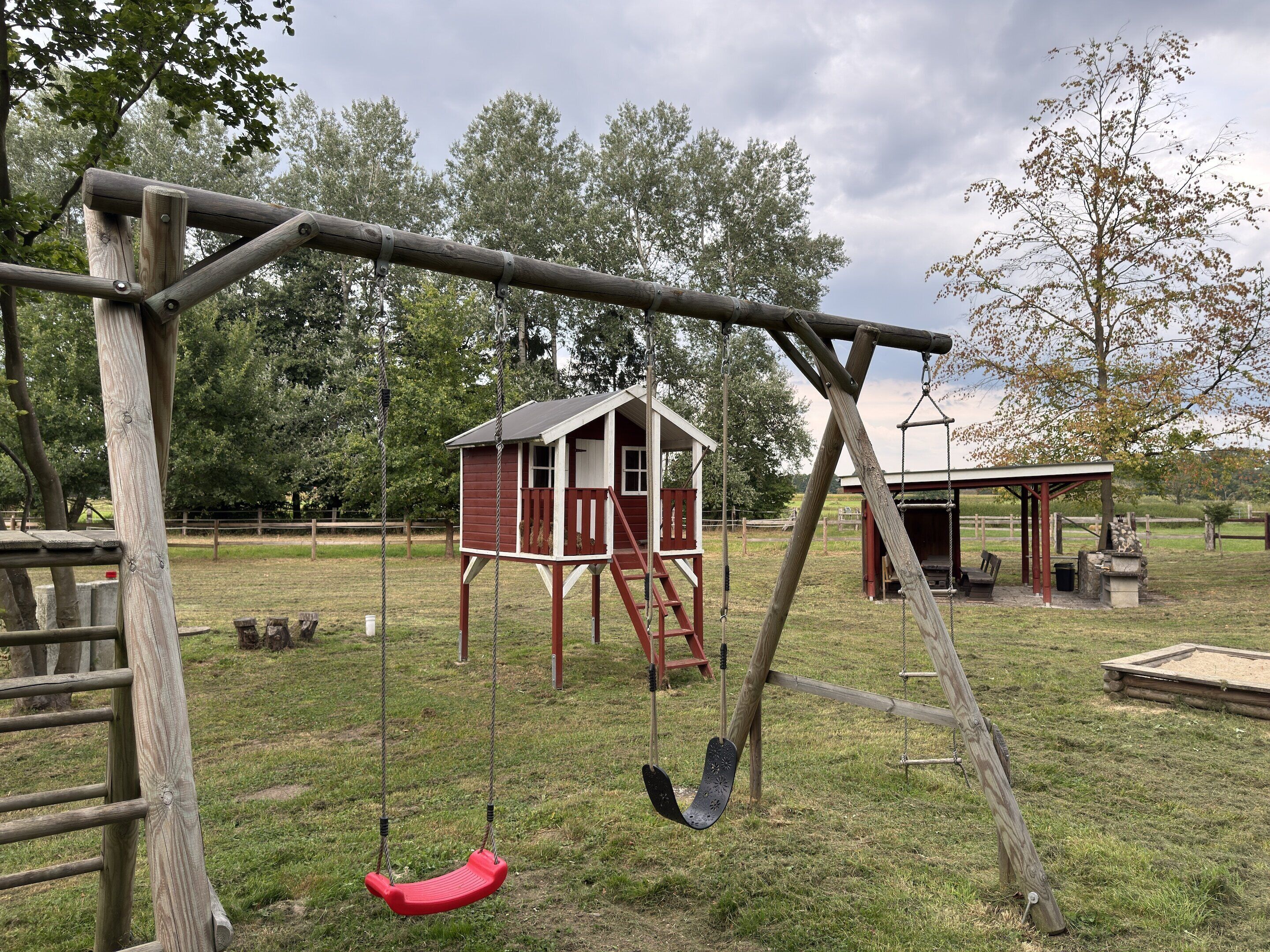 A playground with swings, a red playhouse, and a covered seating area.