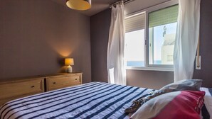 Un dormitori amb un llit, una nituleta, una làmpada i una finestra amb cortines.