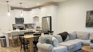 A modern kitchen with white cabinets, a dining area with a wooden table and chairs, a grey sofa, and a ceiling fan. - Back To College! 3 Bed Rooms 2.5 Bathroom- College Street near 280 (Auburn)