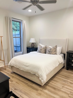 A bedroom with a bed, a ceiling fan, a nightstand with a lamp, a window with curtains, and a wooden floor. - Back To College! 3 Bed Rooms 2.5 Bathroom- College Street near 280 (Auburn)