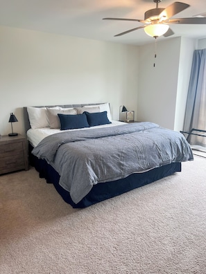 A bedroom with a bed, a nightstand, a lamp, a ceiling fan, and a window with curtains.