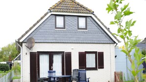 A two-story house with a sloped roof, a satellite dish, and a small patio with two chairs and a table. - Huijsmans Verhuur Type B de Luxe Zuiderdiep 8 (Ouddorp)