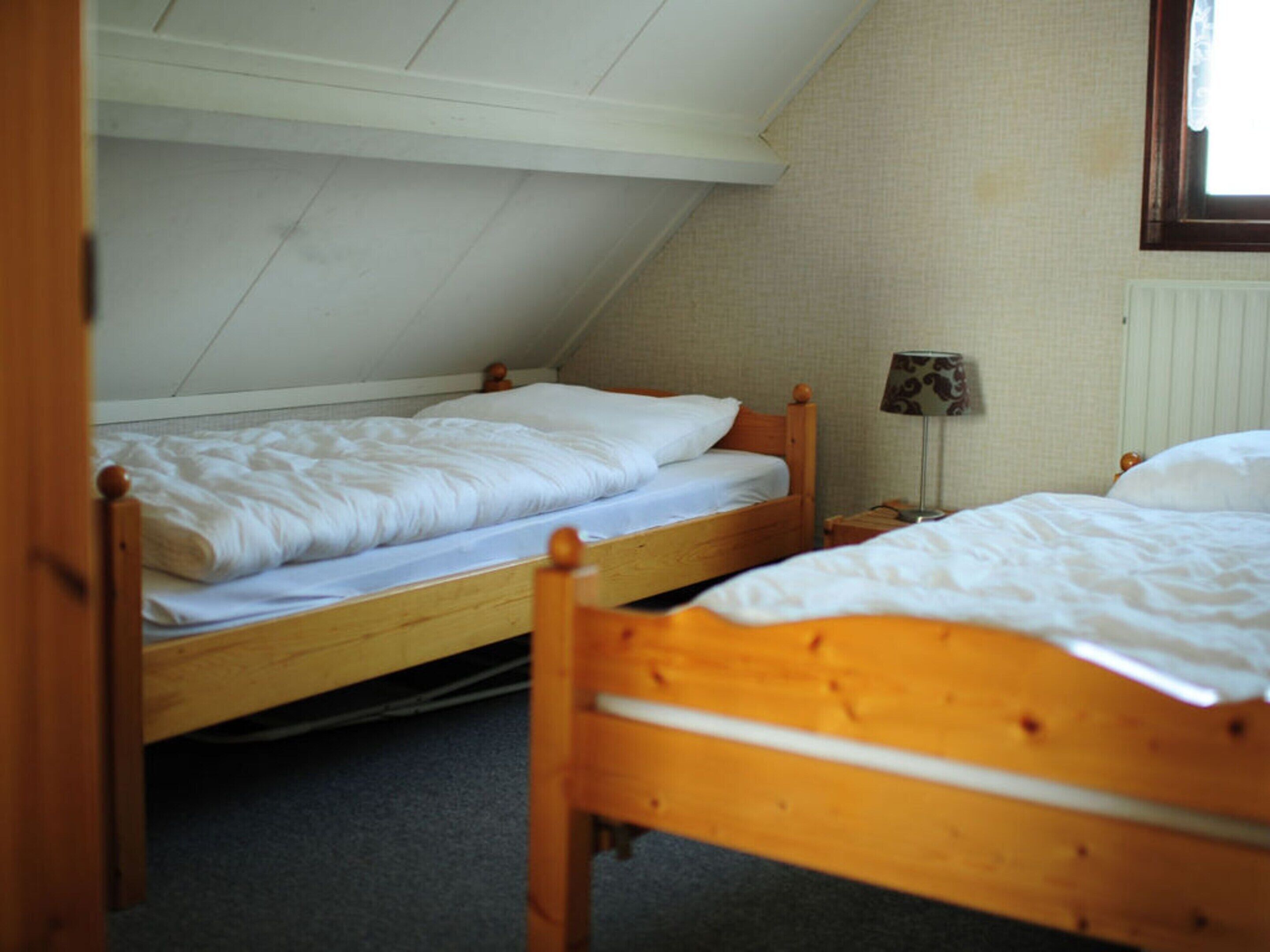 Um quarto de dormitório com duas beliches de madeira, uma pequena mesa de cabeceira com abajur e um radiador na parede.