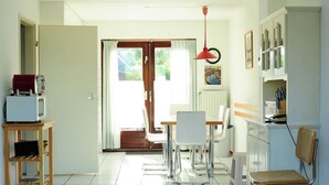 A bright kitchen with white cabinets, a wooden table, and a red hanging lamp. - Huijsmans Verhuur Type B de Luxe Zuiderdiep 8 (Ouddorp)