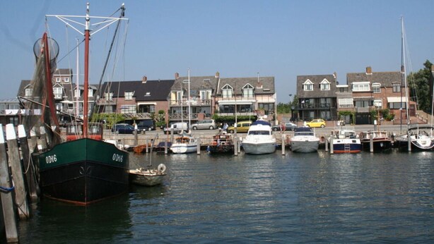 A marina with various boats docked, surrounded by residential buildings. - Huijsmans Verhuur Type B de Luxe Zuiderdiep 8 (Ouddorp)