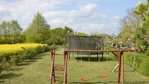 Un columpio de madera en un patio cubierto de césped, con un trampolín y una escalera.