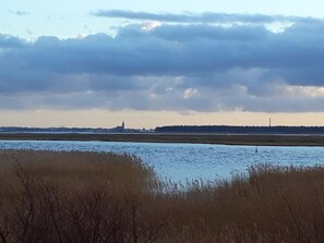 Een kustlandschap met een waterpartij, grasvelden en een gebouw in de verte.