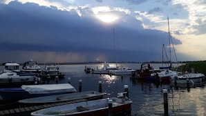 Un puerto deportivo con varias embarcaciones amarradas, agua tranquila y un cielo nublado con rayos de sol.