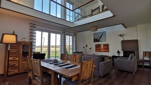 Amplia sala de estar con una mesa de comedor, sillas, un sofá y una chimenea. Una escalera conduce a un nivel superior.