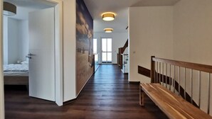 Pasillo de hotel con un banco de madera, una cama en la habitación de la izquierda y un mural en la pared.
