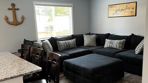 A modern living room with a sectional sofa, a dining area with a kitchen counter, and a ceiling fan. - Cozy Cabin at Villager Resort on Lake Cumberland KY (Somerset)
