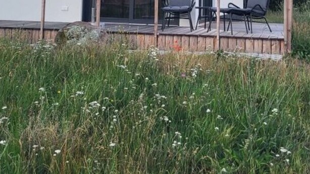 Ein modernes Haus mit einer großen Glasfront, einer Holzdiele und Sitzgelegenheiten im Freien.