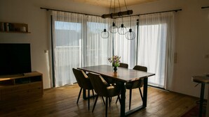 Ein Essbereich mit Holztisch, Stühlen, einer Blumenvase und einem Fernseher auf einer Holzkommode.