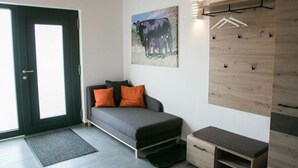 Ein modernes Zimmer mit Schlafsofa, einer Holzwandverkleidung mit Garderobe, einer Tür mit Blick und einem Gemälde von einer Kuh.