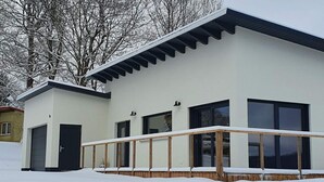 Ein modernes, zweistöckiges Gebäude mit flachem Dach, großen Fenstern und einer Holzterrasse.