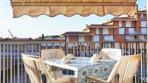 A balcony with a table and chairs, a beige canopy, and a view of buildings in the background. - Apartment in Caorle 500 m From Beach (Caorle)