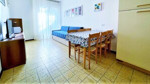 A compact room with a bed, a dining table with chairs, a small kitchenette, and a TV. - Apartment in Caorle 500 m From Beach (Caorle)