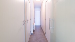 A narrow, well-lit hallway with white walls and a tiled floor, leading to a door at the end. - Cosy Apartment With a Terrace (Middelkerke)