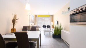 A modern kitchen with a Bosch oven, a dining area with a table and chairs, and a view of the city through large windows. - Cosy Apartment With a Terrace (Middelkerke)