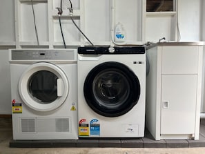 A front-loading washing machine and dryer side by side, with a detergent bottle on top.