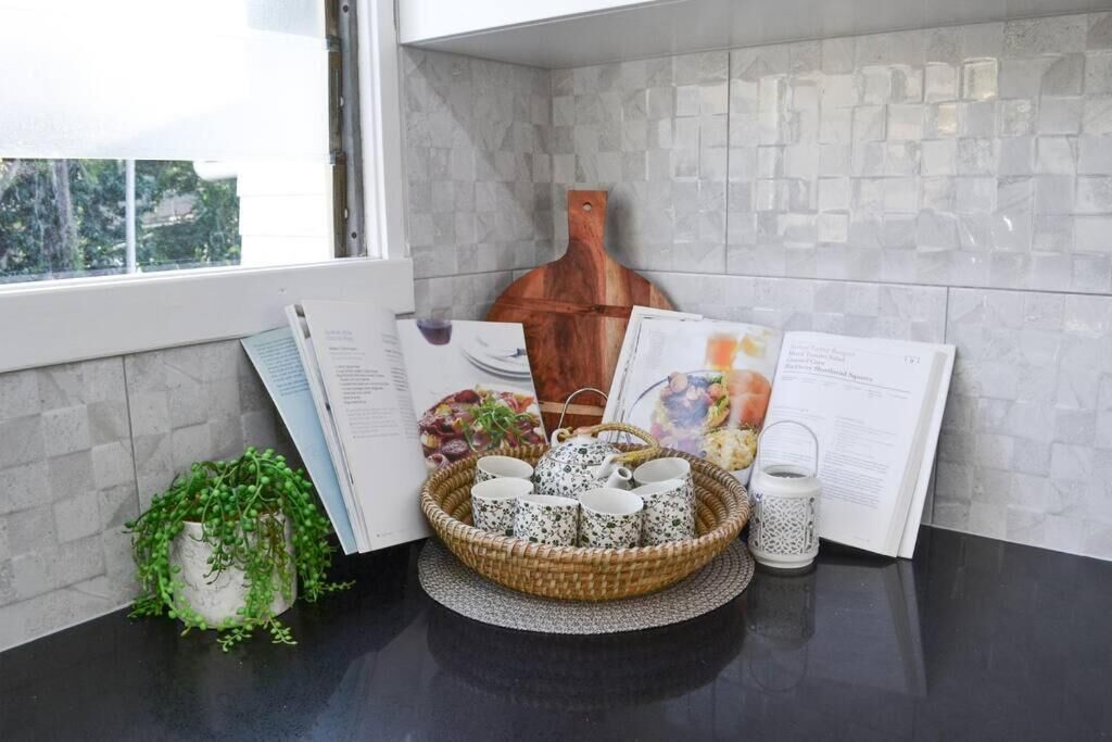 A kitchen counter with a black countertop, a woven basket with cups, a small potted plant, and a book with food images.