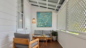 A covered porch with wooden flooring, a grey sofa, a wooden chair, and a table with a plant. - Heritage 5BR Queenslander - Minutes walk to CBD & South Bank (Highgate Hill)