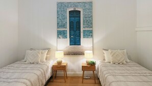 Un dormitorio con dos camas, un cabecero decorativo con una puerta azul y dos mesitas de noche con lámparas.
