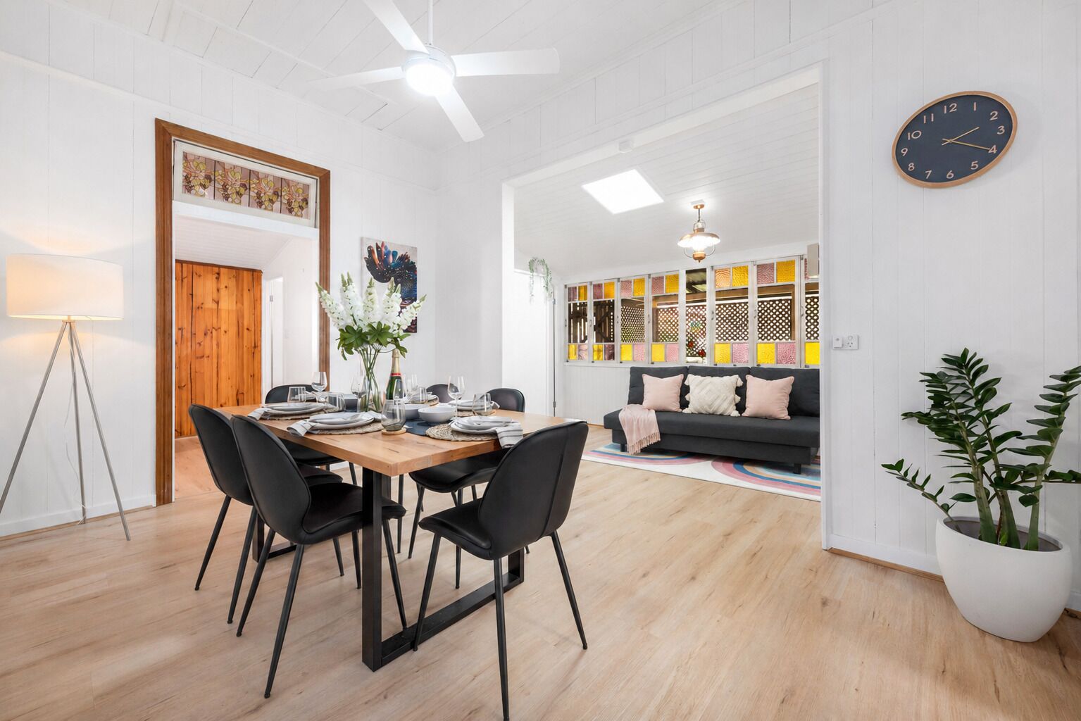 A modern living room with a dining area, a sofa, a clock, and a potted plant.