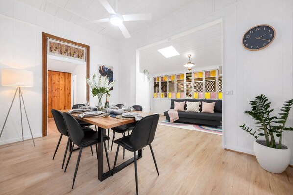 A modern living room with a dining area, a sofa, a clock, and a potted plant.