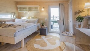 A cozy wooden cabin bedroom with a bed, a small table, a chair, and a view of the outdoors. - Houseboat South Beach (Fehmarn)