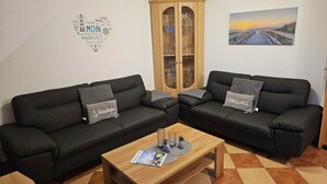 Una sala de estar con dos sofás negros, una mesa de centro de madera y un mueble con puertas de cristal.