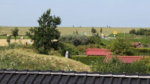 Paisaje rural con campos ondulados, algunos edificios dispersos y un árbol destacado al frente.