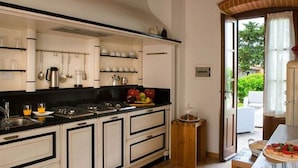 Une cuisine avec des armoires blanches, un plan de travail noir et un plafond en bois. On y trouve un panier de fruits sur le plan de travail et un petit tabouret en bois.