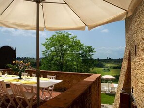 An outdoor dining area with tables and chairs, a large umbrella, and a view of a green landscape and a stone building. - Belvilla by OYO Villa Charme (Barberino Tavarnelle)