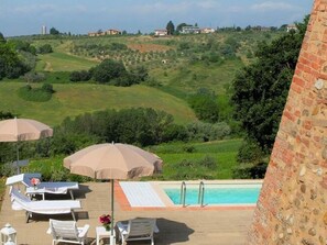 A poolside area with lounge chairs and umbrellas, overlooking a hilly landscape with buildings in the distance. - Belvilla by OYO Villa Charme (Barberino Tavarnelle)