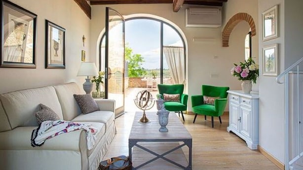 Un salon spacieux avec un canapé, des fauteuils verts et une table basse. Une grande fenêtre offre une vue sur l’extérieur.