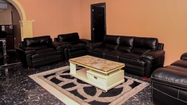 A living room with black leather sofas, a marble floor, and a patterned rug. - Abeokuta 2-Bed House, Sleeps 4 with Free Parking (Abeokuta)