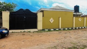 A gated property with a yellow wall and a black gate, a water tank in the background, and a car parked in front. - Abeokuta 2-Bed House, Sleeps 4 with Free Parking (Abeokuta)