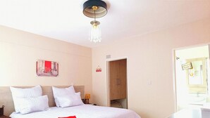 Ein ordentlich bezogenes Bett mit weißer Bettwäsche und einem roten Handtuch, eine Nachttischlampe und eine Tür zu einem Badezimmer.