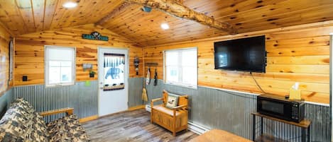 L’intérieur d’une cabine avec un plafond en bois, un téléviseur fixé au mur, un canapé, une petite table et un four à micro-ondes.