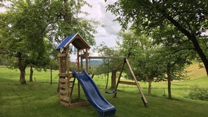 A wooden playground with a slide and swing set in a grassy area with trees. - Holiday Apartment Haus Kirsch (Hilders)