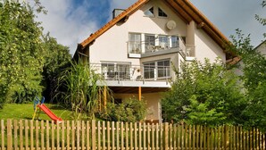 A two-story house with a balcony, a slide, and a wooden fence. - Holiday Apartment Haus Kirsch (Hilders)