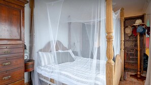 Een hemelbed, een houten dressoir en een schoenenrek met hoeden.