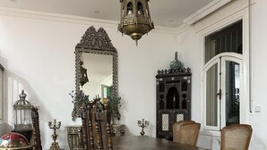 Een eetkamer met een grote houten tafel, sierlijke stoelen, een kroonluchter en een decoratieve spiegel.