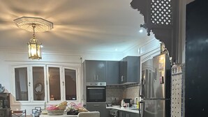Een moderne keuken met donkere kastjes, een ingebouwde oven en een koelkast. Er is een eethoek met een tafel en stoelen, en een decoratieve stoel met een gestreept rugleuning.