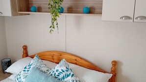 Una cama bien hecha con cabecera de madera, una planta colgante y botes decorativos en un estante superior.
