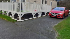 Una casa móvil con un porche blanco y un coche rojo estacionado adelante.
